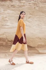 Vestido corto color mostaza con corte evasé y mangas cortas. Presenta un bloque de color marrón en la falda y otro bloque color beige en el ruedo.