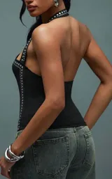 Top negro ajustado al cuerpo con escote asimétrico tipo halter, adornado con tachas plateadas a lo largo del borde del escote y en el lateral derecho.