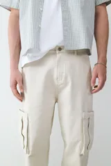 Pantalón cargo beige de corte recto confeccionado en 100% algodón, con múltiples bolsillos delanteros, laterales y traseros.