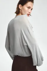 Blusa color marrón con escote en pico, manga larga abullonada con elástico en los puños y volantes en el escote y mangas.
