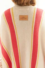 Ruana artesanal color beige con rayas horizontales rojas y amarillas, y flecos en el borde inferior.