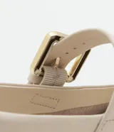 Zapatilla chatita de cuero color crema, con punta redonda, plantilla cómoda y tira con hebilla dorada en la parte superior.