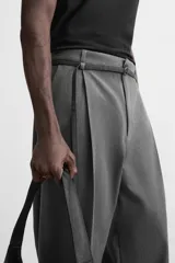 Pantalón gris de corte ancho con pliegues frontales y cinturón fino negro.