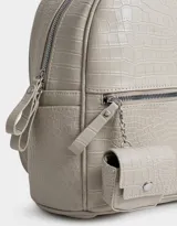 Mochila negra con efecto piel de cocodrilo, bolsillo frontal con cierre, charm de monedero colgante, correas regulables, manija superior, doble cierre superior y bolsillos laterales.