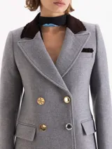 Tapado gris de paño con cuello de gamuza color chocolate. Diseño de doble botonadura con botones metálicos combinados, bolsillos con tapa en el delantero y solapa marcada. Largo hasta la rodilla, corte entallado y hombros levemente marcados.