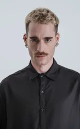 Camisa de manga corta, color negro liso, con cuello camisero y cierre frontal de botones. Corte holgado.