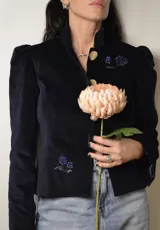 Chaqueta corta de terciopelo azul marino con cuello mao, mangas abullonadas, cierre frontal con botones dorados y bordados florales con cuentas azules.