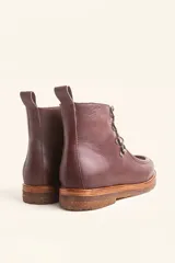 Bota de cuero vacuno color bordó con acabado brillante, diseño tipo botineta con cordones y ganchos metálicos. Presenta suela de goma tipo crepe con plataforma y costuras visibles en la puntera.