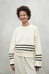 Sweater color crema con rayas horizontales negras en el pecho y los puños, de corte holgado y cuello redondo.