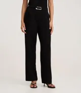 Pantalón de vestir color crudo, de corte recto, con bolsillos laterales y traseros. Se ajusta a la cintura con cinturón de cuero marrón con hebilla dorada.