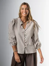 Camisa de lino a rayas marrones y blancas, con leve hombro princesa y manga abullonada.