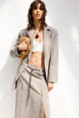 Falda midi de lino color gris con textura. Tiene tiro alto, cinturón fino del mismo tejido y abertura frontal. Cierre lateral con cremallera oculta.