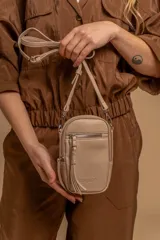 Bandolera compacta de símil cuero color beige, con correa regulable y desmontable. Presenta un bolsillo frontal con cierre, un bolsillo trasero sin cierre y un bolsillo interior forrado en tela.