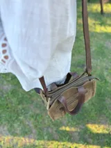 Cartera bandolera de cuero color verde oliva, con forro de tela, bolsillo delantero con cierre y bolsillo interno. Tiene correa larga regulable y manijas cortas.