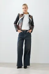 Chaqueta corta de cuero sintético color negro, marrón y blanco, con cuello de piel sintética blanca, cierre frontal con cremallera y bordados en las mangas.