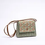 Bandolera verde tejida con hilo de yute, con solapa con diseño geométrico en tonos beige y verde, cierre con botón a presión y correa larga de cuero marrón.