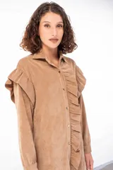 Camisa larga color beige de pana fina con cuello camisero, cierre frontal con botones y mangas largas con puños abotonados. Presenta volados en los hombros y a lo largo del cierre frontal.