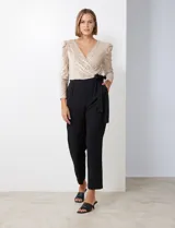 Enterito de fiesta con torso de lentejuelas color champagne, escote en V cruzado, mangas 3/4 con frunces en los hombros, cintura elastizada con lazo negro y pantalón negro de corte recto con bolsillos laterales.