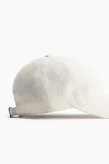 Gorra color crudo confeccionada en mezcla de algodón y ramio, con cinta antitranspirante de tela, trabilla ajustable con cierre de metal en la parte posterior.