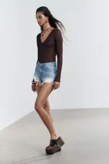 Shorts de denim negro con tiro medio, cinco bolsillos y efecto desgastado con roturas pronunciadas y bajo deshilachado.