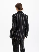 Blazer de jacquard negro con rayas verticales formadas por pequeños estampados de labios. Presenta solapas con vivo, bolsillo relojero y cierre frontal con broche snap dorado.