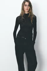 Pantalón de jean negro con efecto lavado, tiro alto, corte carrot fit, cintura elástica en la parte trasera, bolsillos delanteros y traseros, cierre frontal con cremallera y botón metálico.