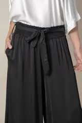 Pantalón palazzo negro de rayón y viscosa, con cintura elastizada, lazo y bolsillos laterales.