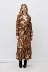 Vestido largo de viscosa estampada en tonos marrón y beige, con escote en V, mangas largas con puños elásticos y volado en el ruedo. Incluye lazo del mismo género para ajustar en la cintura.