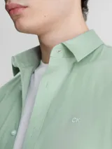 Camisa verde claro de popelín elástico, corte slim, con cierre frontal de botones, mangas largas y logo de Calvin Klein bordado en el pecho.