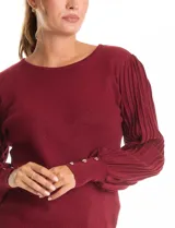 Buzo de tejido lurex marca Nanette en color bordó, con cuello a la base y mangas largas de diseño plisado. Los puños cuentan con apliques de botones decorativos.