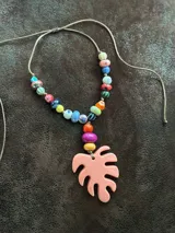 Collar corto con cuentas de cerámica y acrílico de colores, tiento sintético y dije de resina en forma de hoja de palmera color coral.