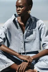 Camisa corta de denim celeste, con cuello solapa, manga larga, bolsillo delantero de plastrón y cierre frontal con botones metálicos.