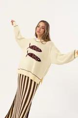 Sweater color manteca de tejido de punto con cuello redondo y ribete marrón. Presenta dos peces marrones tejidos en el frente con detalles bordados a mano.