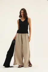 Pantalón de lino color beige, de corte ancho, con cintura elástica y ribete negro en los laterales con tajos en el ruedo.