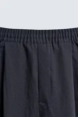Pantalón negro de corte relajado con cintura elástica ajustable y pliegues en la parte delantera. Presenta bolsillos laterales y bolsillos traseros de parche.