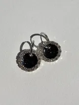 Aros colgantes con argolla de acero quirúrgico y dije circular de resina negra con borde de strass plateado.