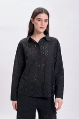 Camisa negra de manga larga con cuello clásico y cierre con botones. Presenta bordado tipo broderie con calados circulares. Corte recto.
