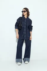 Pantalón de jean de tiro bajo, color azul oscuro, con rayas verticales blancas y silueta ancha (wide leg). Presenta costuras contrastantes y dobladillo ancho doblado hacia afuera.