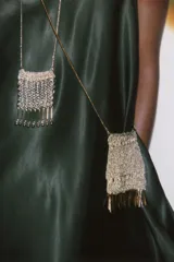 Bolso mini tipo saco confeccionado con hilo metalizado color dorado en forma de malla. Detalle de flecos metálicos labrados. Asa tipo cordón metálica.