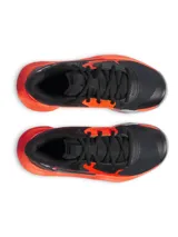Championes de básquet Under Armour UA GS Jet 23, color negro con detalles en naranja y suela gris. Presentan capellada de malla transpirable y entresuela Micro G para amortiguación.
