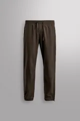 Pantalón de jogging color marrón oscuro, corte regular fit, confeccionado en tejido técnico ligero y elástico. Cuenta con cintura elástica ajustable con cordón, bolsillos frontales con cierre de cremallera, bolsillo trasero con cierre de cremallera oculta en costura y bajo ajustable con elástico.