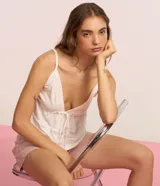 Blusa blanca de algodón y poliéster con breteles finos, escote en V con lazo ajustable y detalles de recortes decorativos.