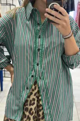 Camisa de popelina de algodón con rayas verticales verdes, blancas y oscuras. Presenta una abertura frontal pronunciada con ribete de festón verde y botones negros.