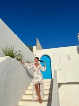Vestido corto blanco con estampado floral en tonos naranja y verde, escote en V con detalle de nudo, mangas largas acampanadas y falda con volantes y abertura lateral.