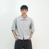 Camisa de hombre de corte boxy fit, con estampado de rayas verticales en tonos grises y blancos, confeccionada en gabardina de algodón. Presenta cuello clásico, mangas cortas y bordado con el logo de la marca en la espalda.