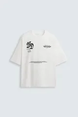 Camiseta blanca de corte holgado, cuello redondo y manga corta. Presenta estampados combinados en negro en la parte delantera y trasera.