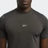Remera deportiva gris oscuro de manga corta, con logo reflectante de Reebok en el pecho y paneles de malla en hombros y laterales.