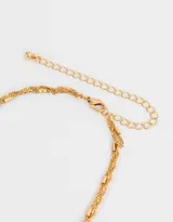 Collar corto multicadena bañado en oro con dije de cruz y dije de cristal.