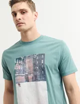 Remera color petróleo de manga corta con estampa de un edificio y texto en el frente.