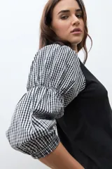 Remera de cuello redondo en color negro con mangas tres cuartos abullonadas que presentan un estampado de cuadros Vichy en blanco y negro.